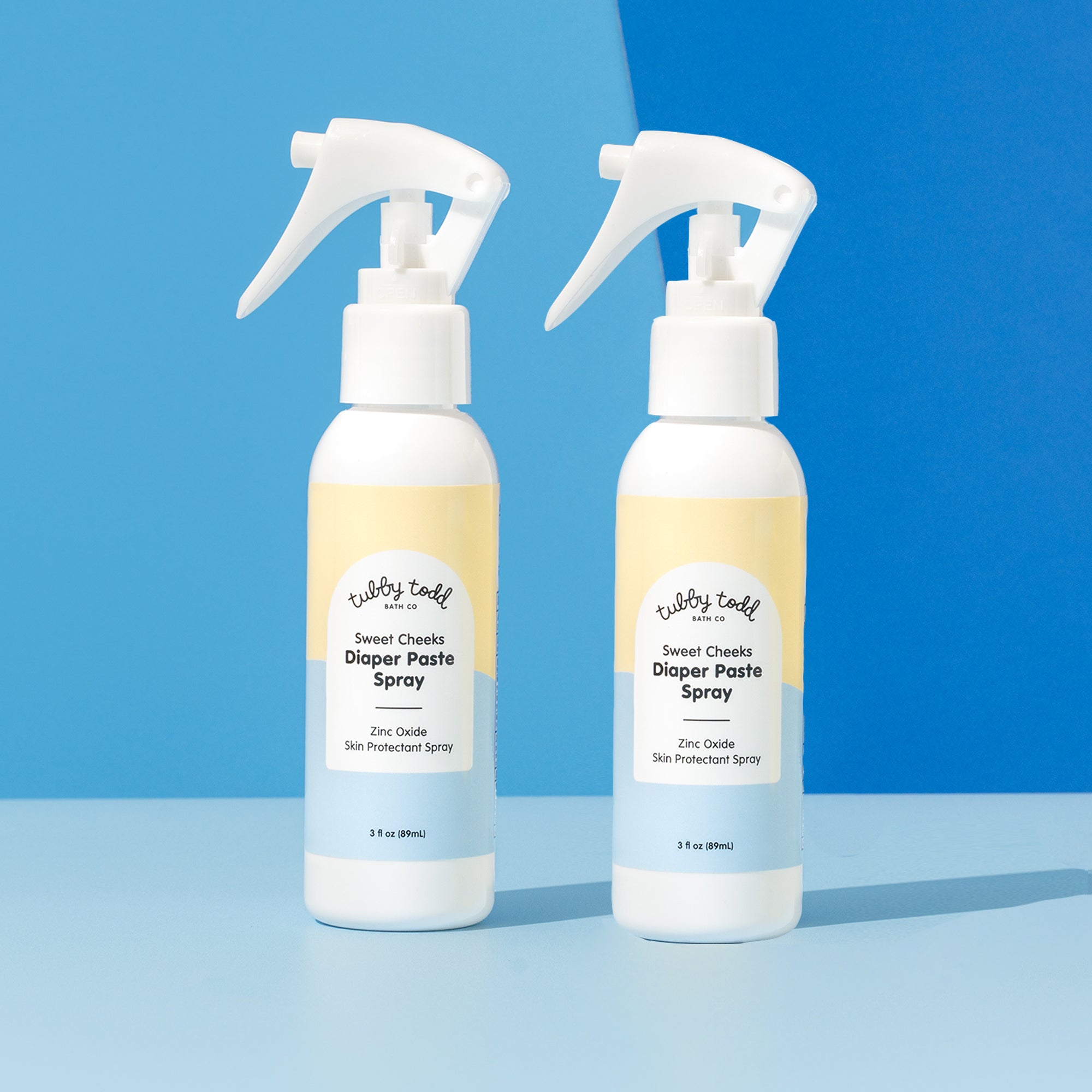 2 Diaper Paste Spray products are standing on the color block background.
